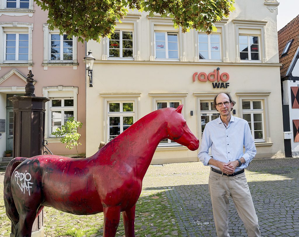 Frank Haberstroh, Chef­redakteur von Radio WAF, steht neben einer roten Pferdeskulptur. Im Hintergnd ist das Redaktionsgebäude zu sehen.