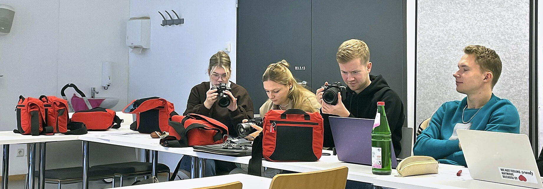 Vier Sudierende beschäftigen sich in einem Seminarraum mit Kameras und Zubehör.