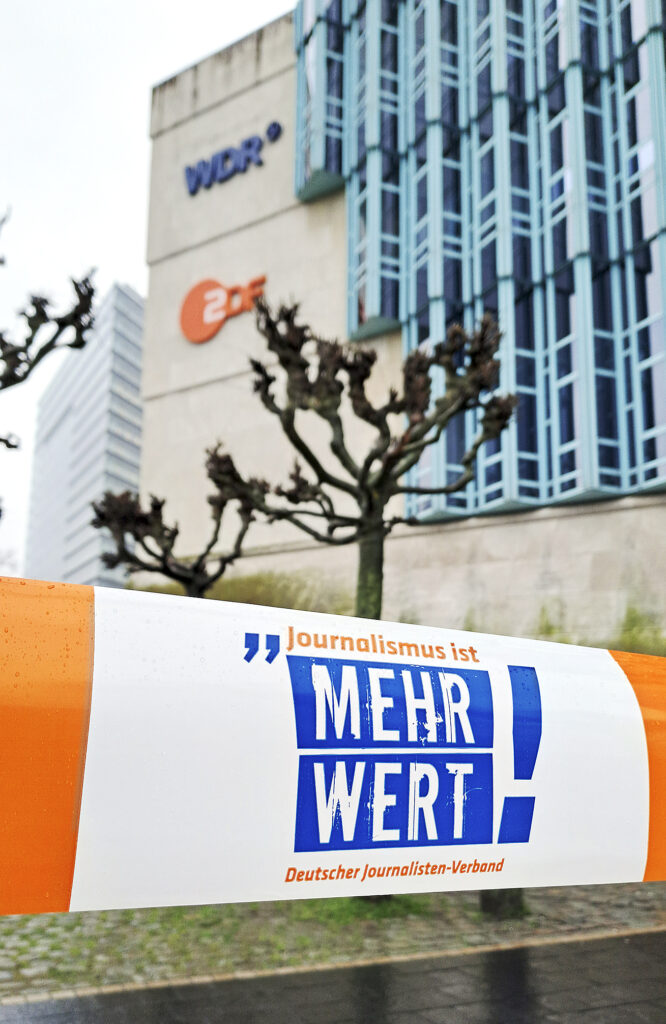 Vor dem Düsseldorfer Studio von WDR und ZDF ist ein Flatterband gespannt. Die Aufschrift: Journalismus ist mehr Wert! Deutscher Journalisten-Verband