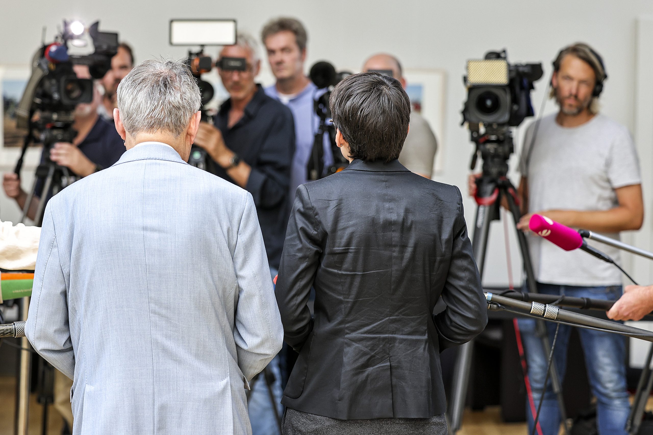 Ein Mann und eine Frau von hinten, vor Ihnen, mit dem Gesicht zum Betrachter, mehrere Kameraleute. 