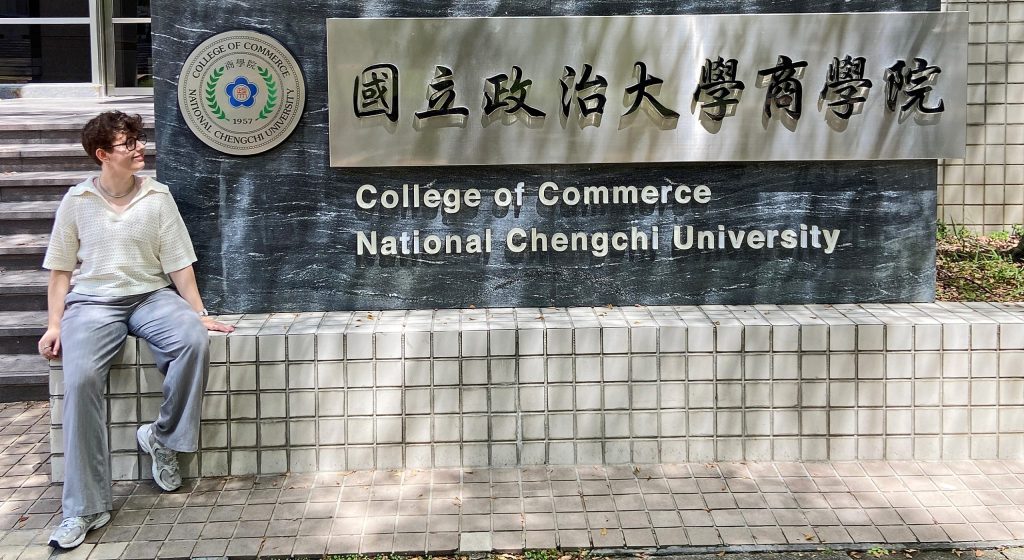 Die Autorin sitzt neben einem Schild der Universität in Taipei, an der sie ein Auslandssemester macht.