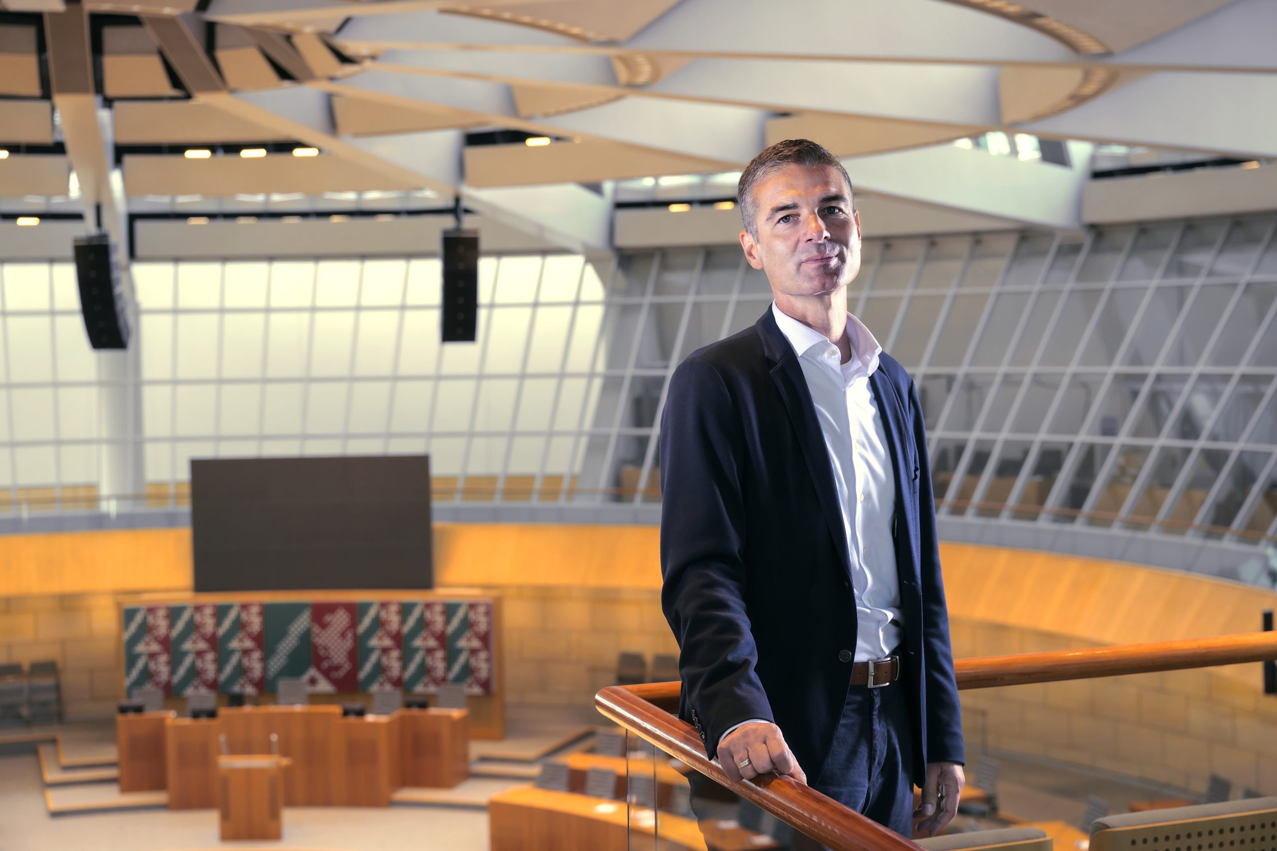 Ein Mann steht im leerem NRW-Landtag und schaut in die Kamrea.