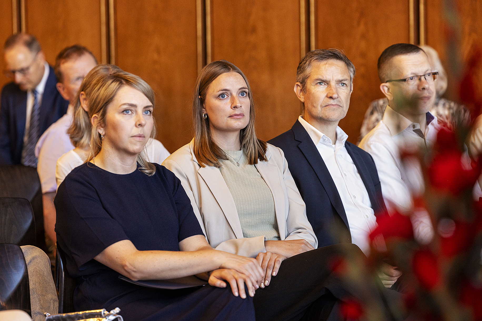 In einem repräsentativen Saal sitzen zwei Frauen und zwei Männer nebeneinander. sie lauschen offensichtlich einer Rede. 