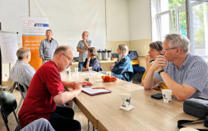 Ein heller Raum, in dem Menschen an einem großen Tisch sitzen und arbeiten.