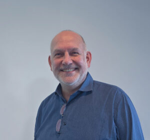 Ein Mann lächelt in die Kamera. Er trägt ein blaues Hemd