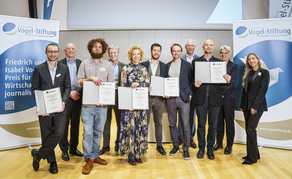 Eine Gruppe von Personen steht auf einer Bühne, diejenigen, die ausgezeichnet wurden, halten ihre Urkunde vor dem Bauch.