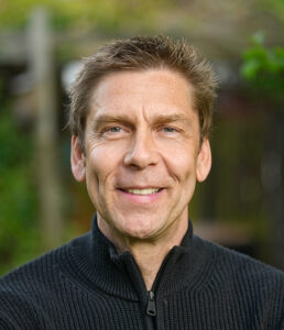 Außenaufnahme eines lächenden Manns in einem schwarzen Oberteil