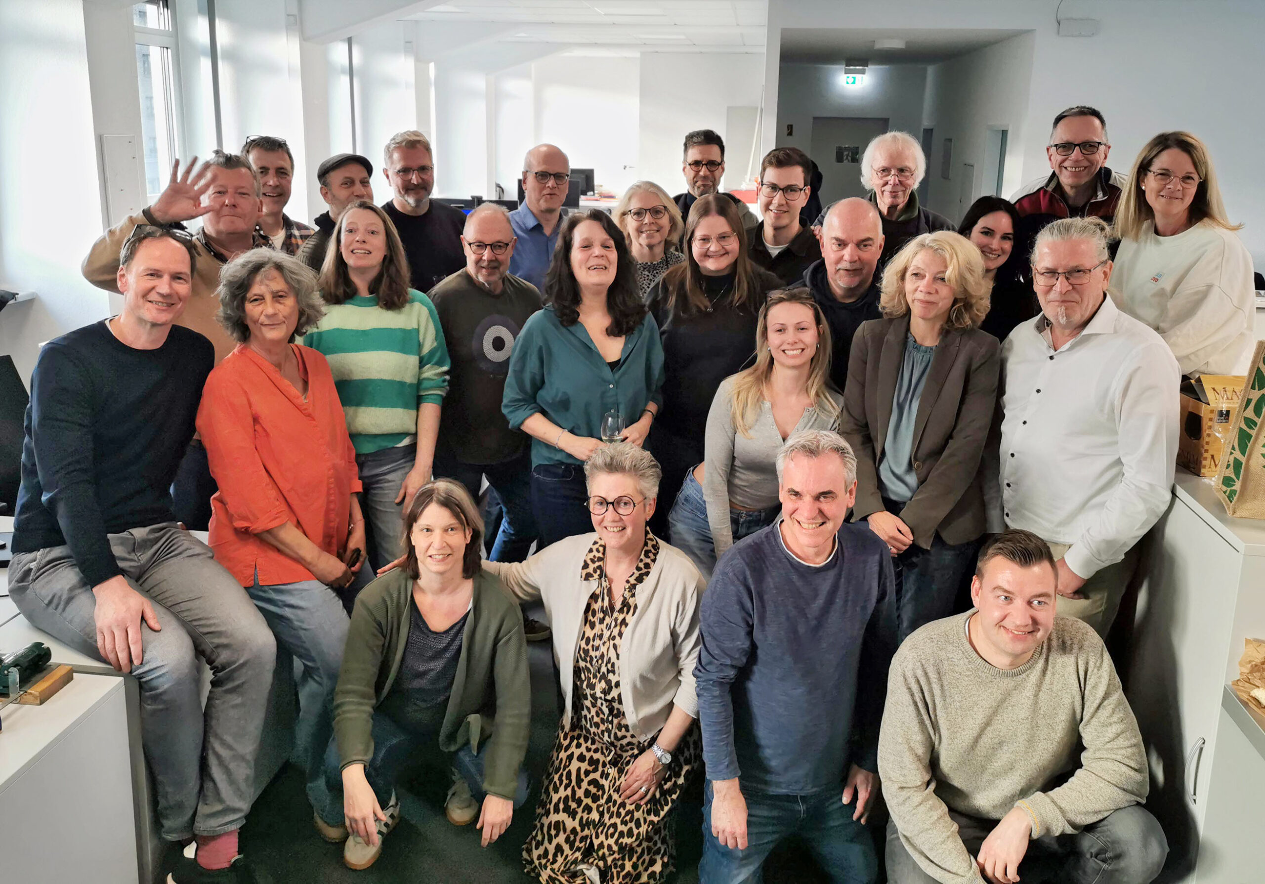 Eine Gruppe von rund 25 Menschen hat sich für ein Abchiedsfotot gestaffelt aufgestellt, hinten hebt einer die Hand und winkt.