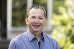 Außenaufnahme eines lächelnden Manns in einem hellblauen Hemd.