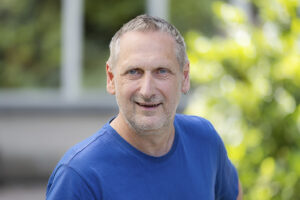 Außenaufnahme eines lächelnden Manns in einem blauen T-Shirt.