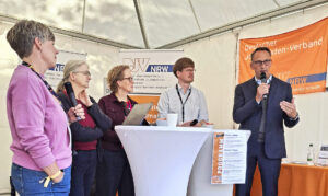 Drei Frauen und zwei Männer stehen um einen Stehtisch, einer der Männer spricht in ein Handmikro. Im Hintergrund zwei Banner mit dem Logo des DJV-NRW.