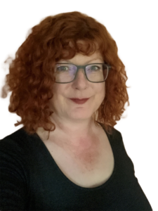 Ein Frau mit roten Locken und Brille lächelt seitlich in die Kamera.